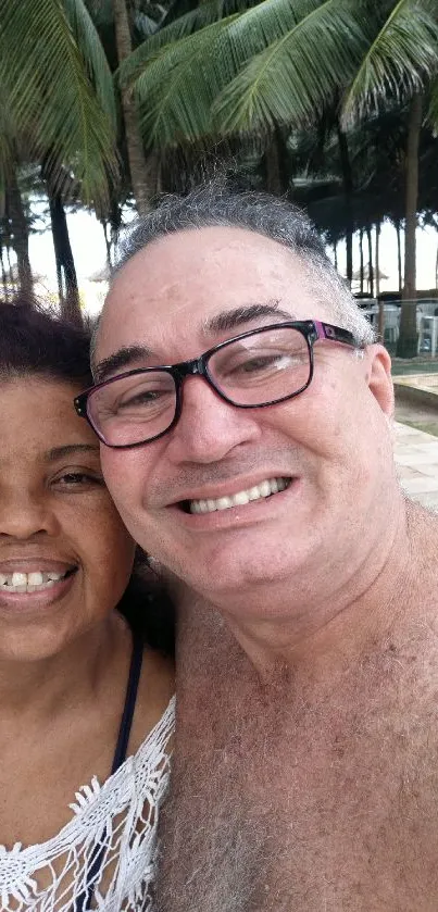 Couple smiling at tropical beach with lush palm trees.