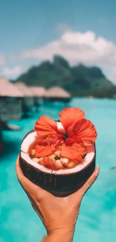 Hand holding coconut with hibiscus on turquoise sea background.