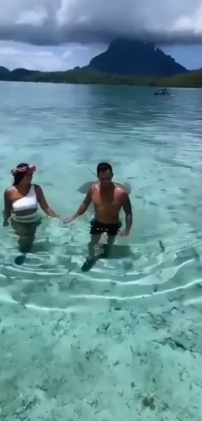 Couple strolling in turquoise waters with island backdrop.