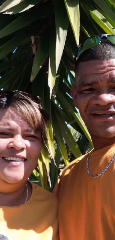 Couple in yellow shirts against green tropical background.