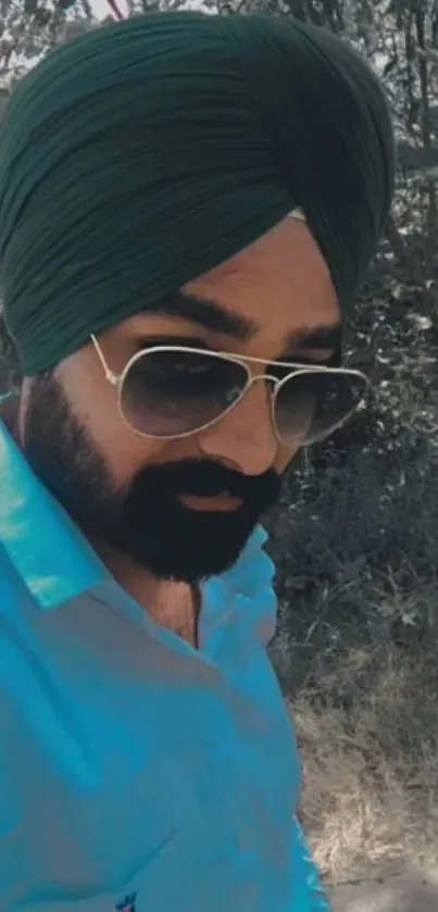 Man in dark green turban and sunglasses in a natural setting.