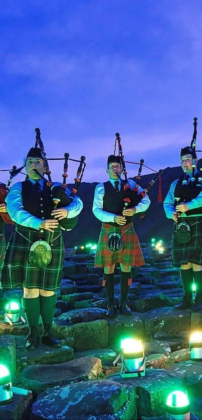 Bagpipers in kilts under a twilight sky with green lights.