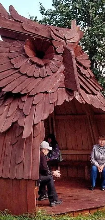 A wooden owl-shaped hut in a green nature setting with people inside.