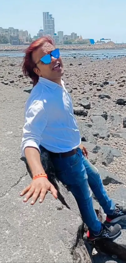 Person relaxing on a rocky beach with cityscape in the background.