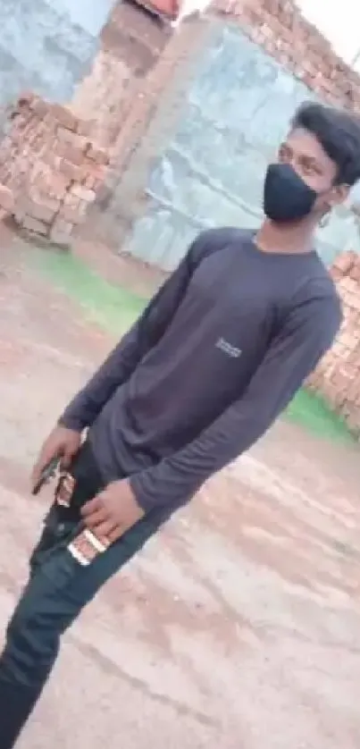 Young man in black mask stands in brick yard.