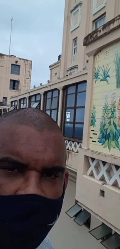 Man with mask in front of mural on urban building.