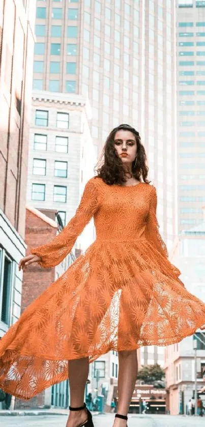 Woman in orange lace dress standing in urban cityscape.