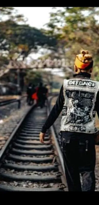 A person walking alone on railway tracks amid trees and a rustic bridge.