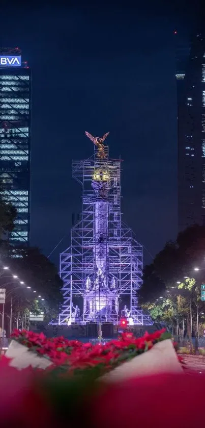 Illuminated statue on urban night street with skyscrapers.