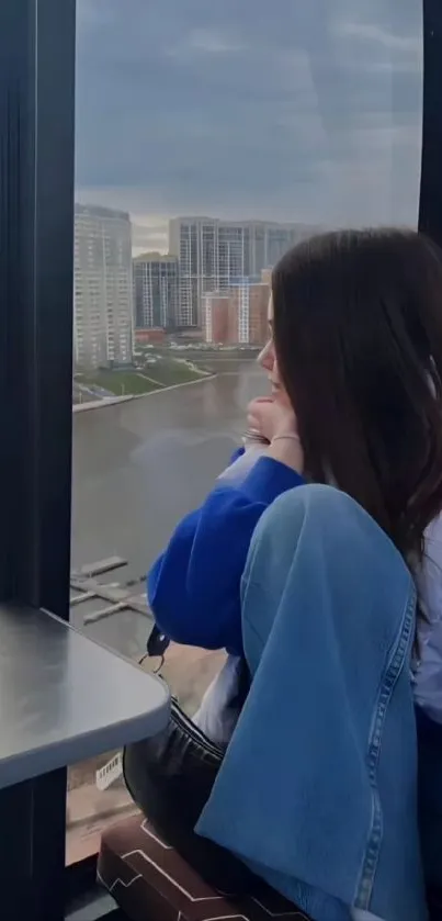 Woman in blue jacket looking over cityscape from window.