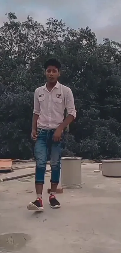 Young man on rooftop with trees and cloudy background.