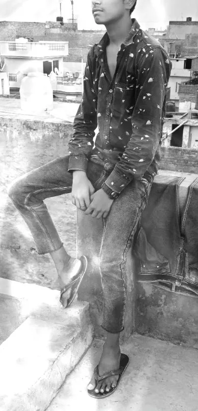 Young man sits casually on an urban rooftop in monochrome.