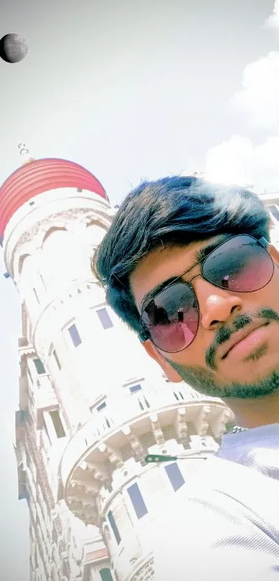 Stylish man in sunglasses taking a selfie in front of a historic tower under a clear sky.