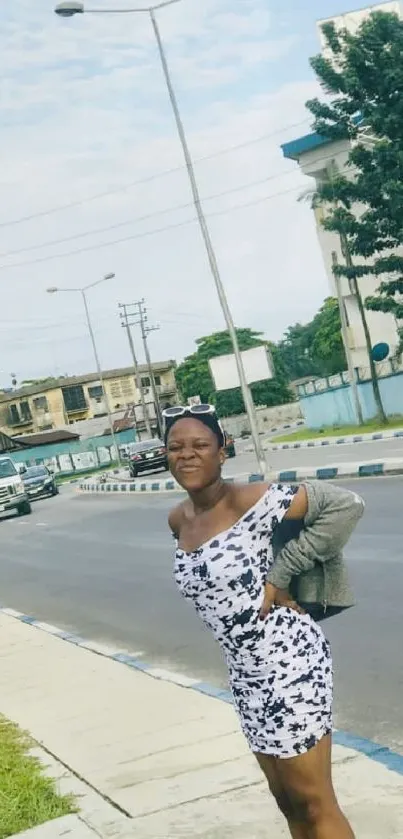 Woman in a patterned dress on an urban street with greenery.