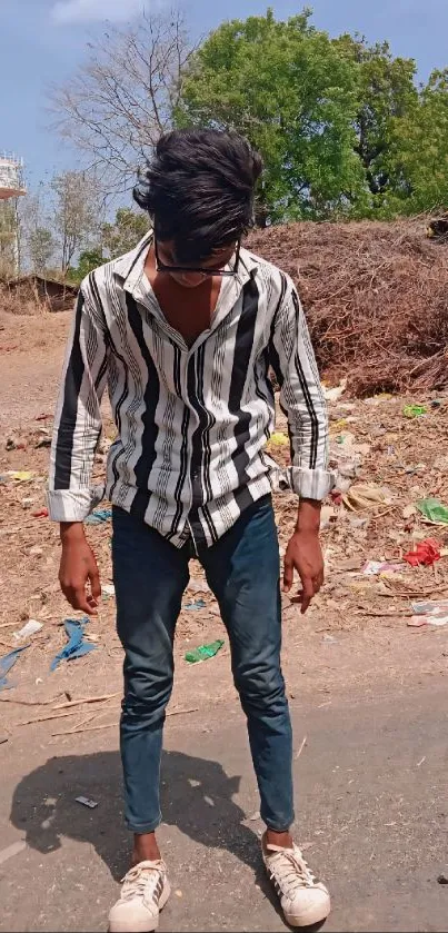 Young man in striped shirt standing outdoors on a sunny day.