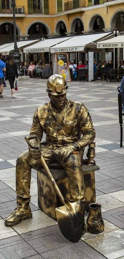 Street performer in gold paint on urban plaza with onlookers.