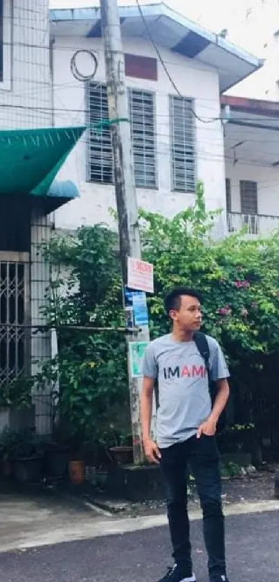 Man standing on an urban street with greenery and buildings.