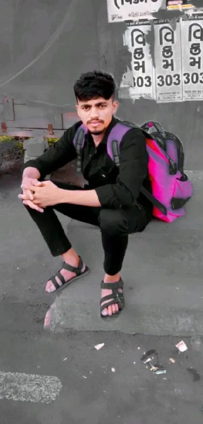 Man sitting on sidewalk in urban style with pink backpack.