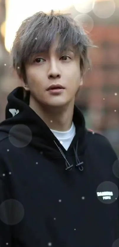 Young man in urban setting with gray hoodie, city backdrop and soft lighting.