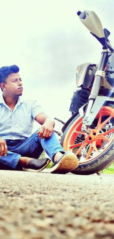 Man sitting by a motorcycle with vibrant wheels on a scenic road.