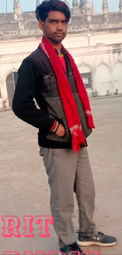 Man with red scarf stands outdoors beside historic building.