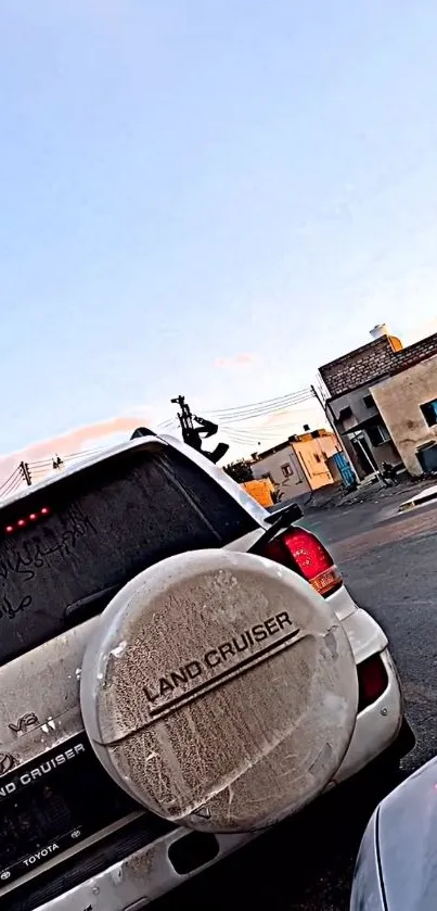 White Land Cruiser on urban street with buildings and blue sky.