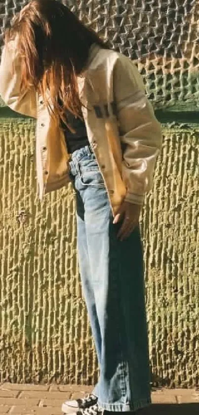 Young woman in a casual outfit poses against a textured urban wall.