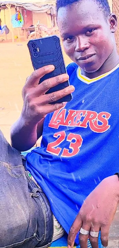 Young man in blue jersey holding a smartphone.