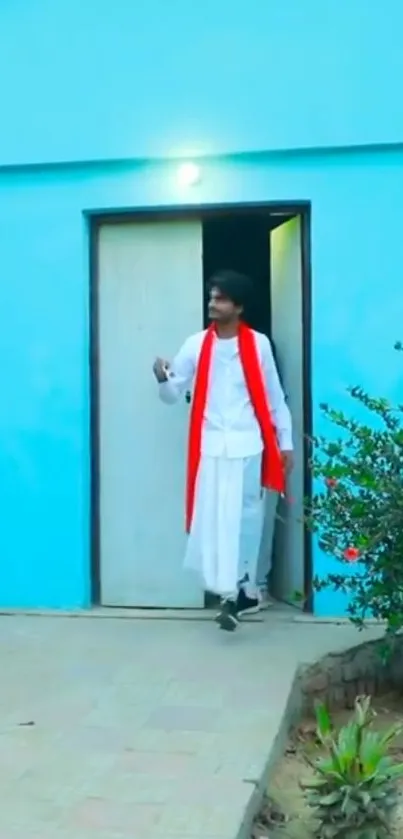 Man in traditional attire exiting a vibrant turquoise building.