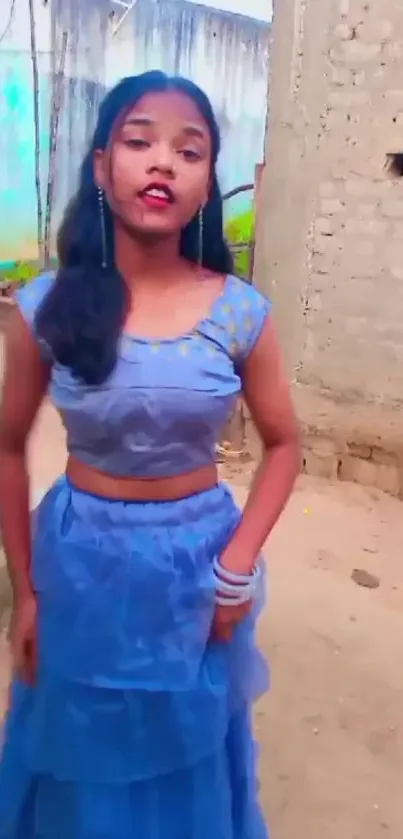 Young woman in blue dress against rustic backdrop.