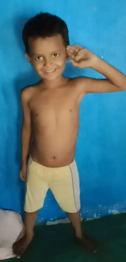 Smiling child in front of a vibrant blue wall.