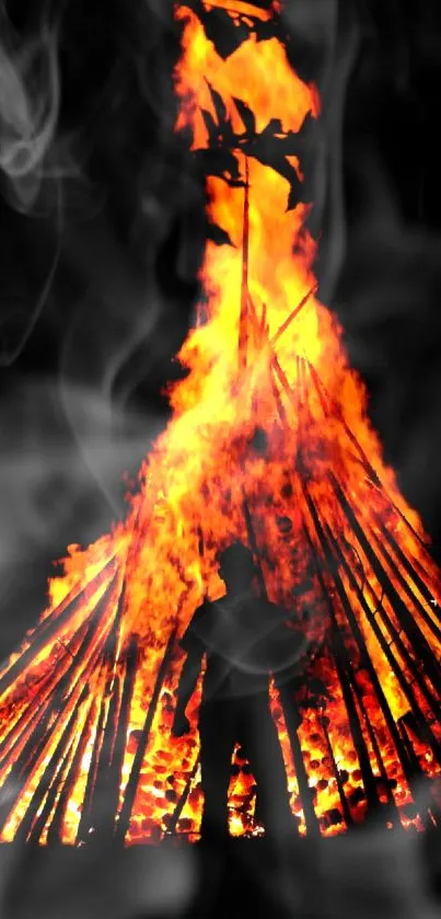 Silhouette in front of a blazing bonfire with smoke against a dark background.