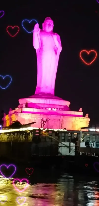 Buddha statue glows pink at night by a riverside.
