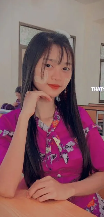 Young woman in magenta floral dress posing in classroom.