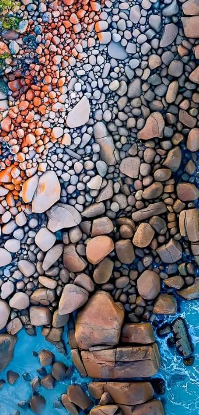 Aerial view of colorful stones meeting blue ocean waves on a coastline.