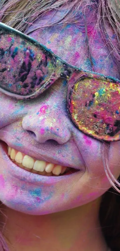 A smiling face covered in colorful Holi powders with vibrant sunglasses.