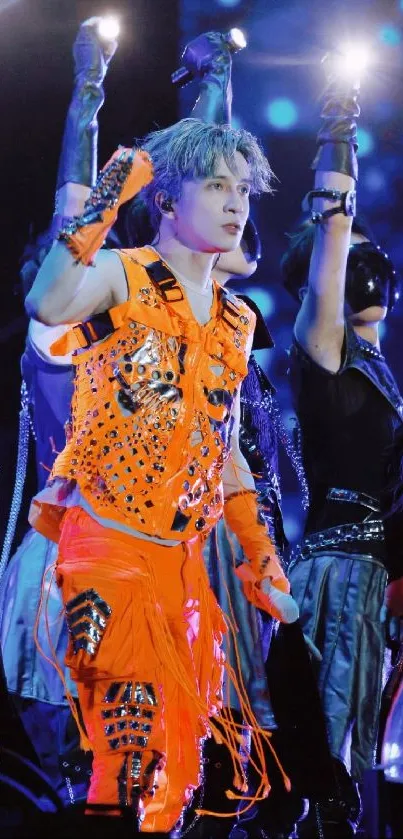 Performer in vibrant orange outfit on stage with dynamic lighting.