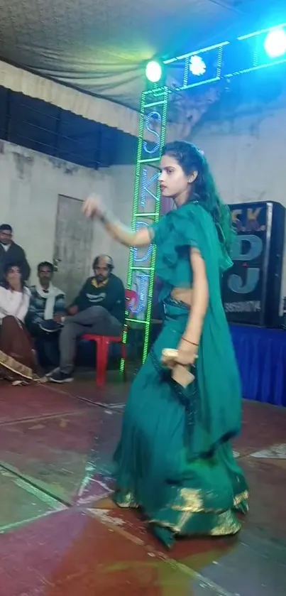 Woman in teal dancing at a cultural event with vivid lights.