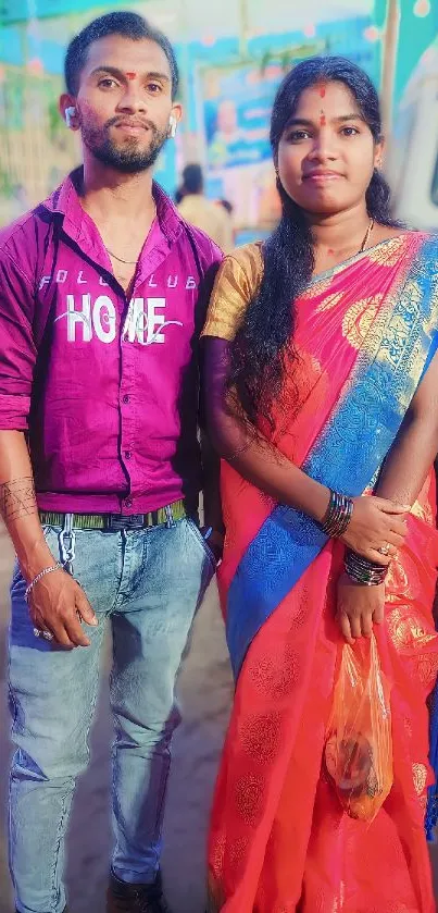 Traditional couple in vibrant attire at a cultural festival with colorful decor.