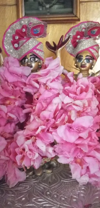 Deity statues adorned with pink flowers and vibrant decor.