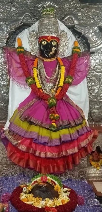 Intricate deity statue adorned with vibrant colors and floral offerings in a temple.