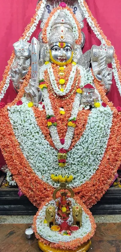 Floral adorned deity statue with vibrant red background and intricate details.