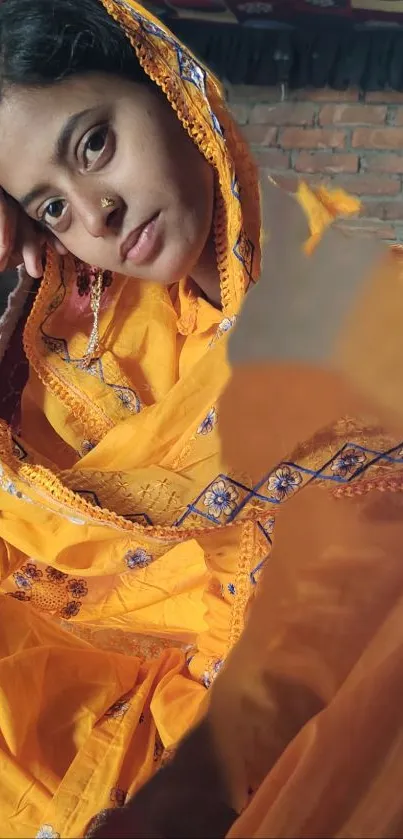 Woman in vibrant orange traditional attire with brick backdrop.