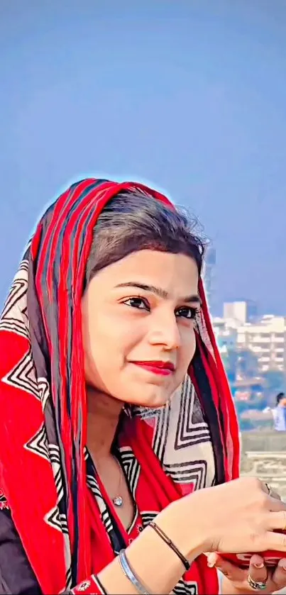 Portrait of woman with vibrant red and black ethnic attire against city backdrop.