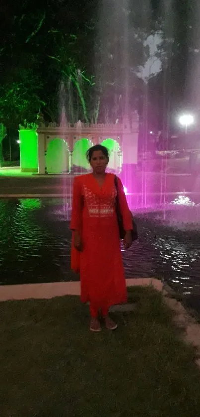 Woman standing by a fountain with colorful night lights in a serene evening setting.