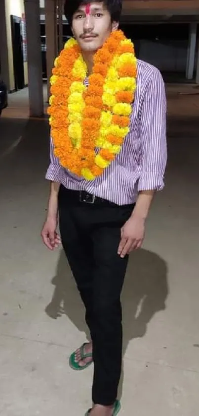 Person adorned with marigold flower garland standing in a parking area.