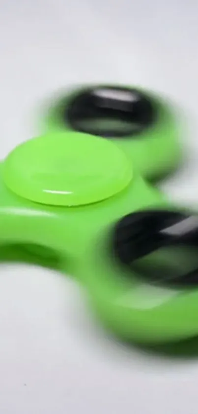 Vibrant green fidget spinner with black accents on a mobile wallpaper.