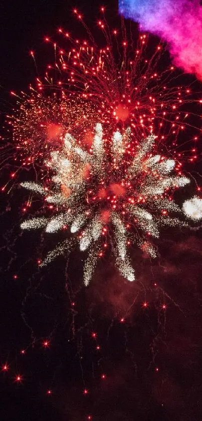 Red fireworks and multicolored burst illuminate the night sky.