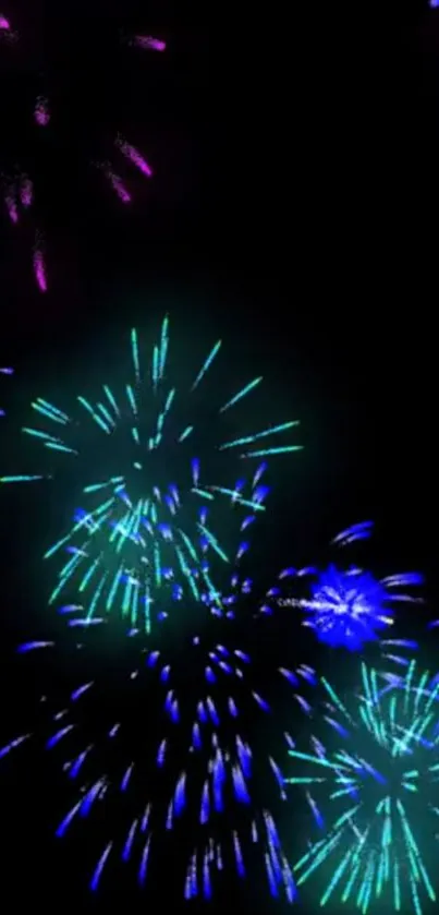 Vibrant fireworks illuminate a dark night sky with blue and green bursts.