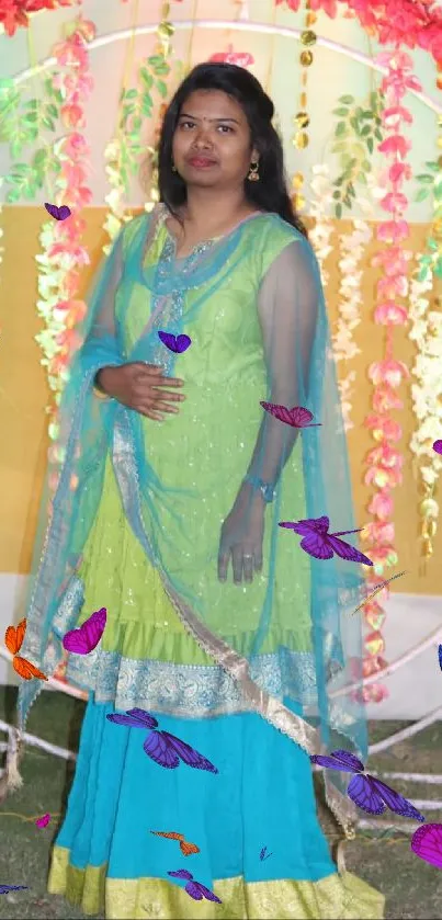 Woman in traditional turquoise attire with vibrant floral backdrop.